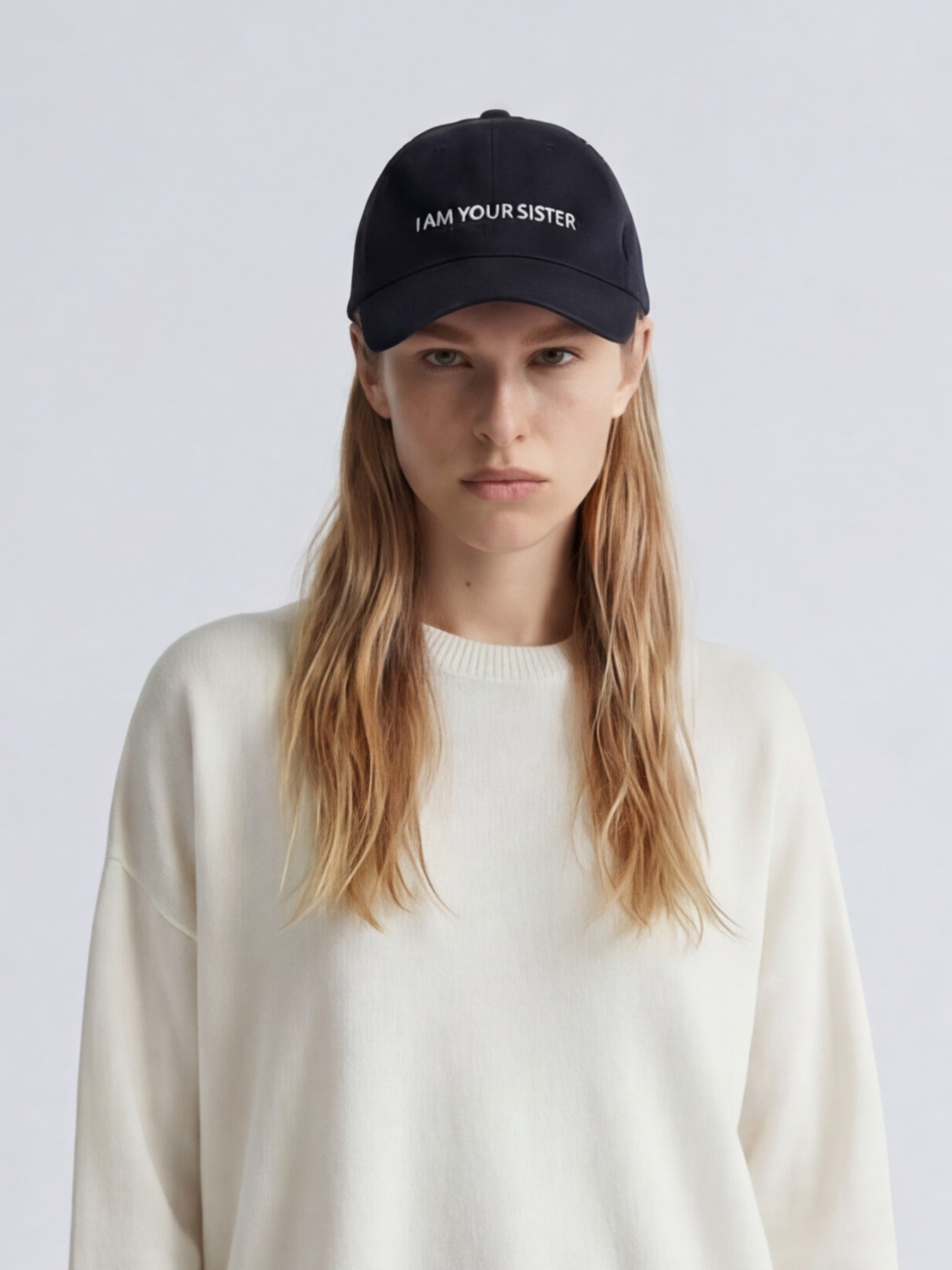 Woman wearing a black cap with 'I AM YOUR SISTER' text on a white background