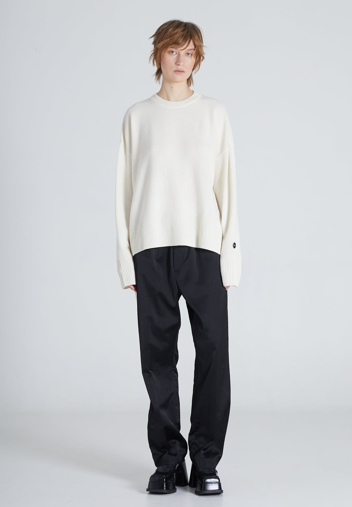 Woman is wearing a white cashmere sweater and black pants on a light gray background