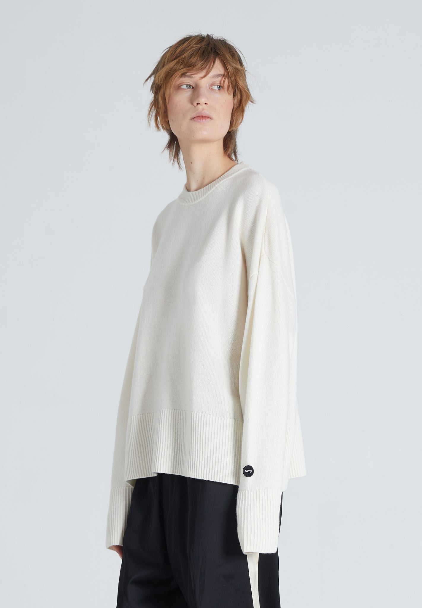 Woman wearing white cashmere crewneck. She is also wearing black trousers. 