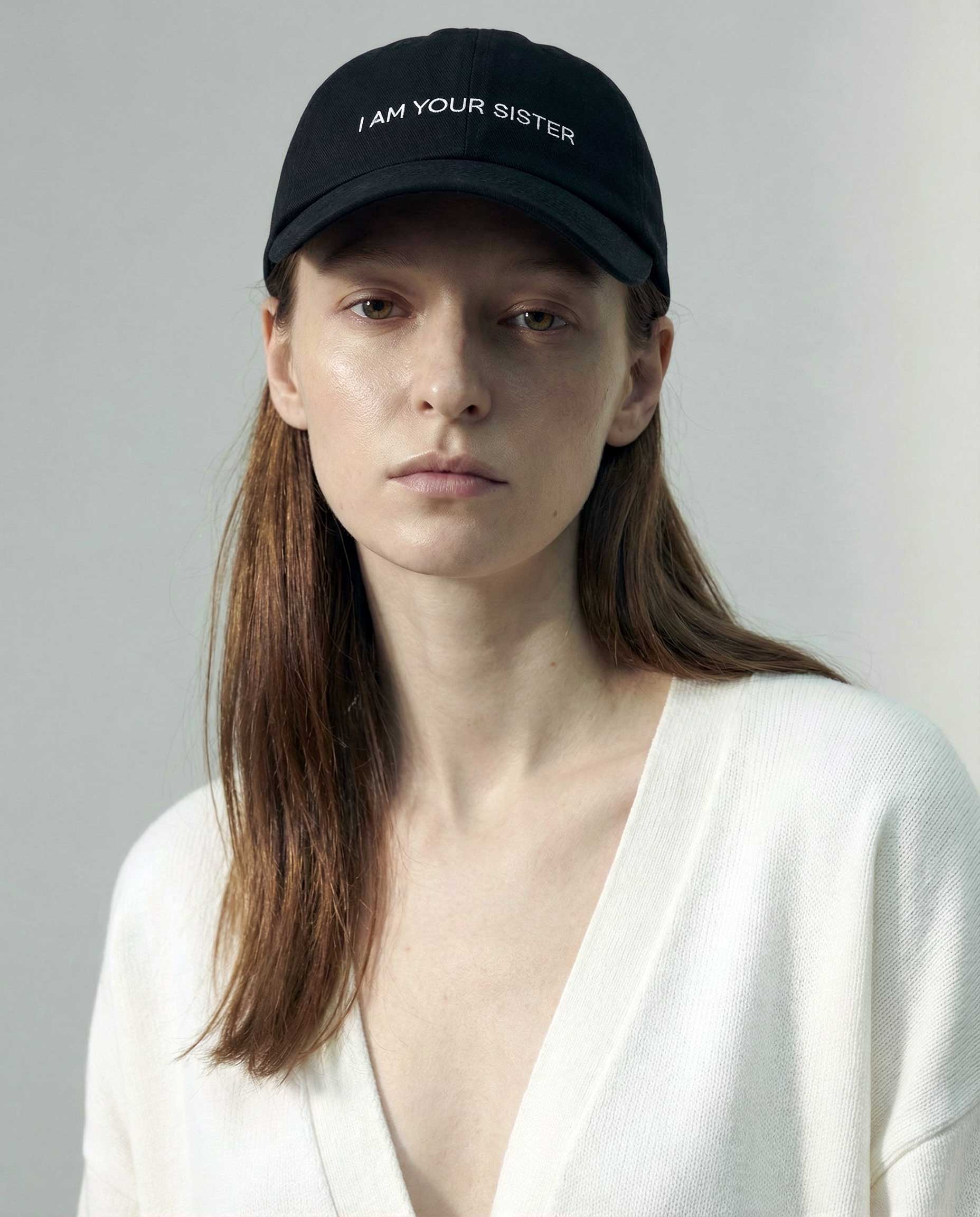 Woman wearing a black cap with 'I AM YOUR SISTER' text on a plain background