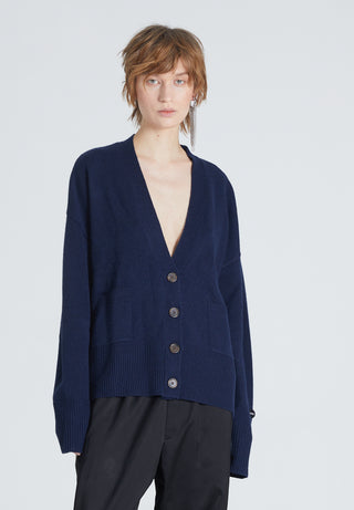 A woman wearing a navy v-neck cardigan with front button-up closure and front pockets, against a dark background.