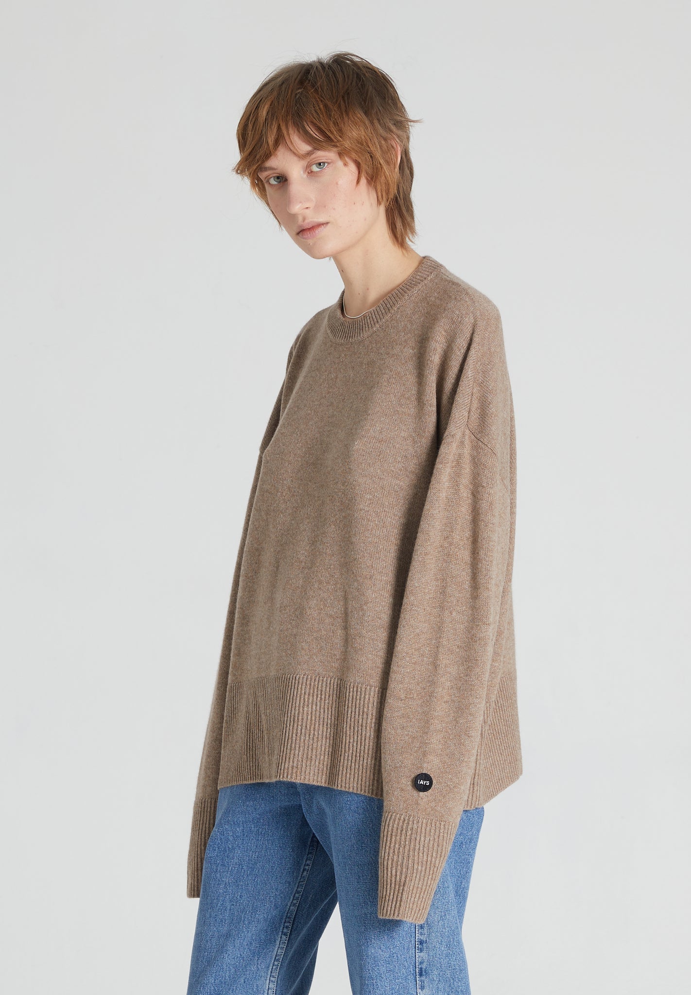 A female model wearing a brown cashmere crew neck long-sleeve sweater and blue jeans.