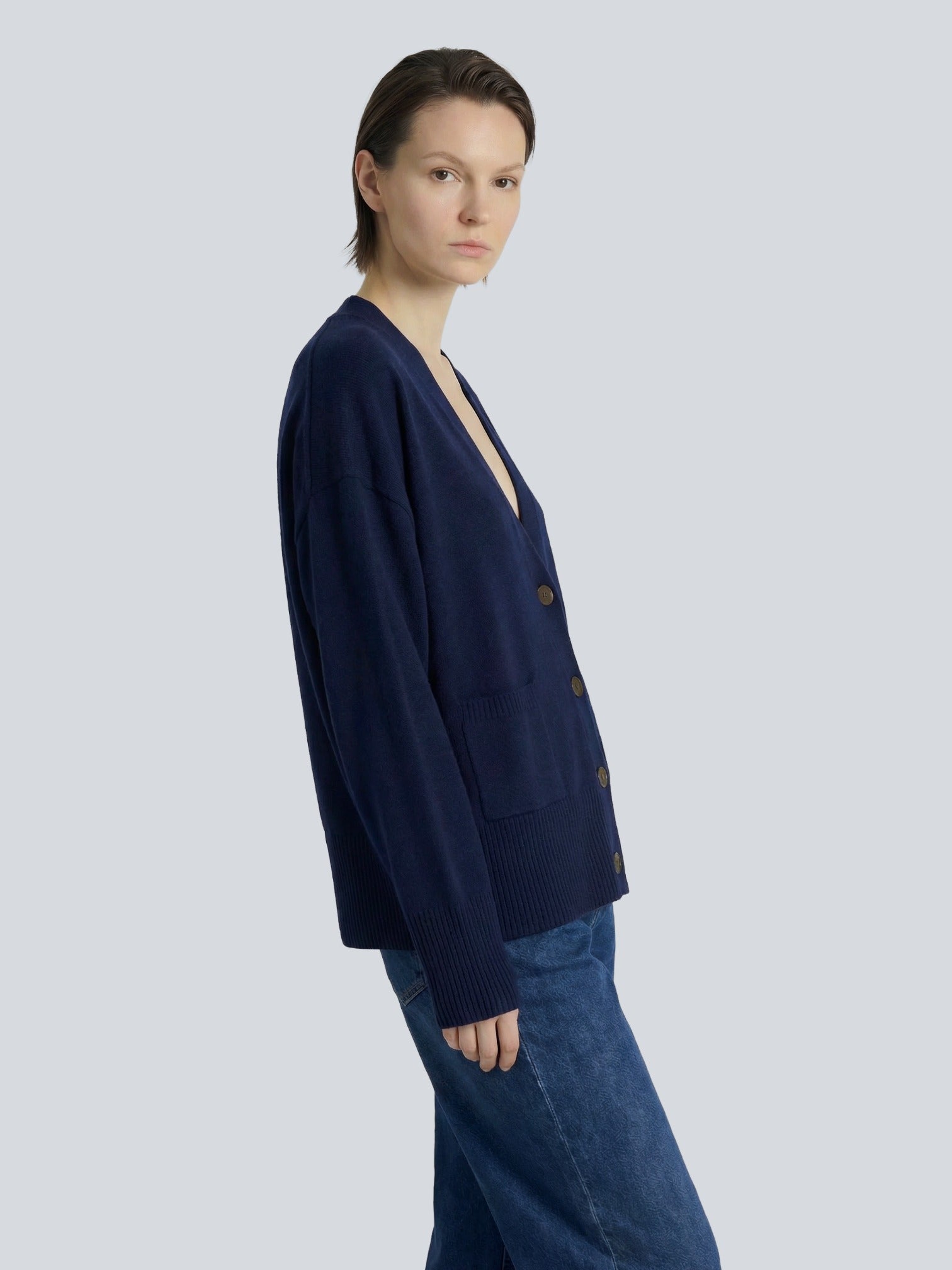 Woman wearing a navy blue Cashmere cardigan and jeans on a light gray background