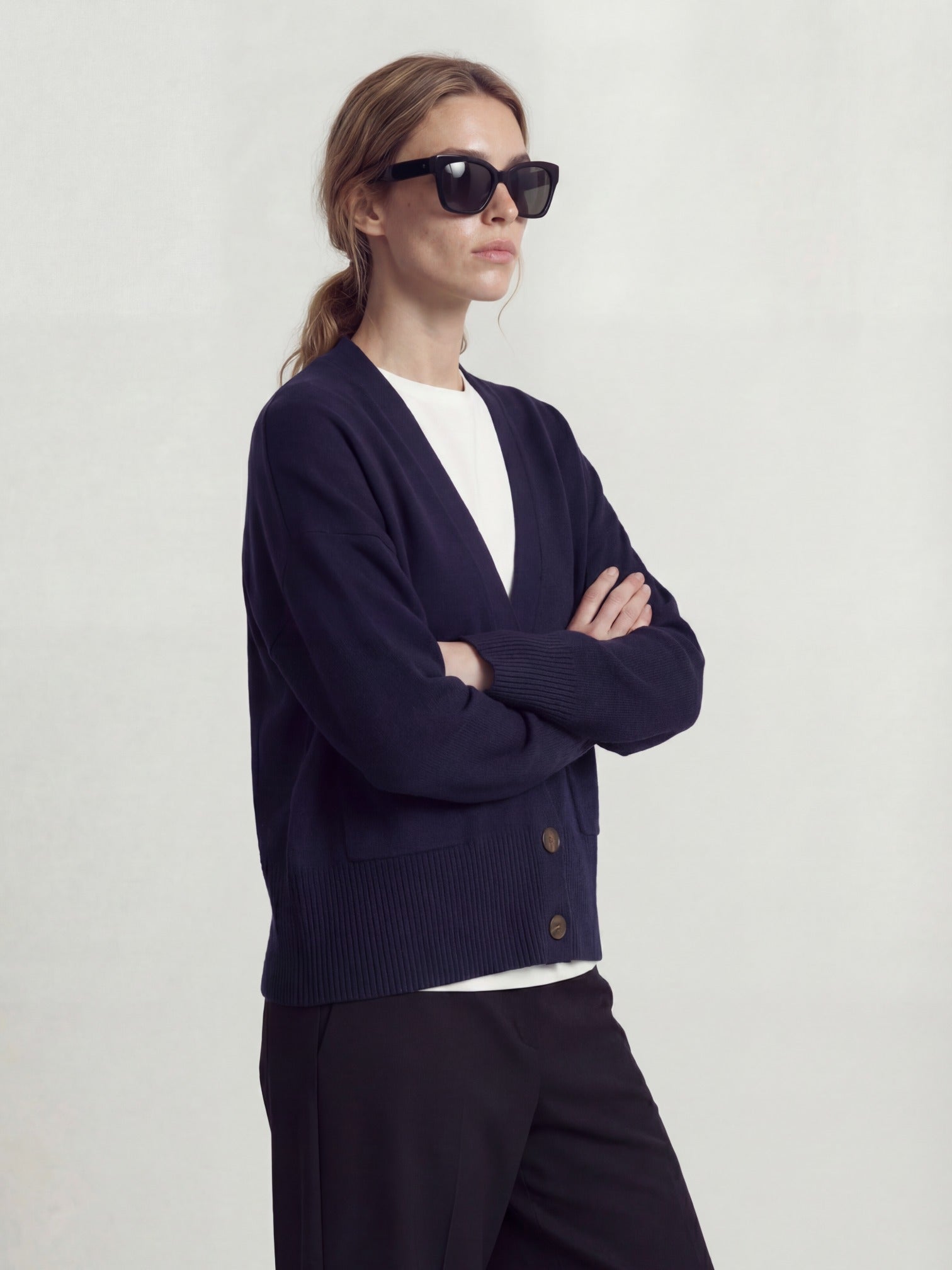 Woman is wearing a navy cashmere cardigan and sunglasses on a plain background
