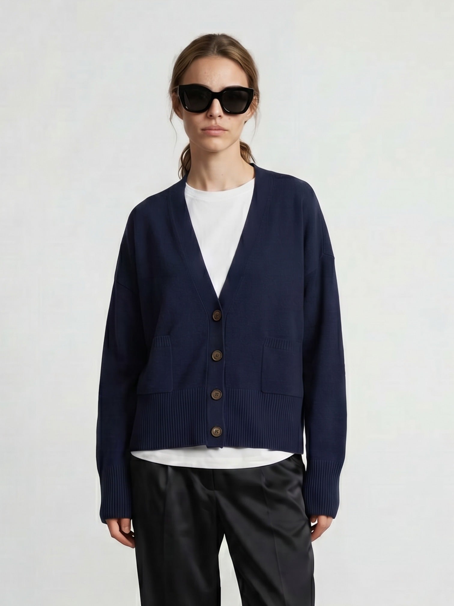 Woman wearing a navy cashmere cardigan over a white shirt with black pants on a light gray background