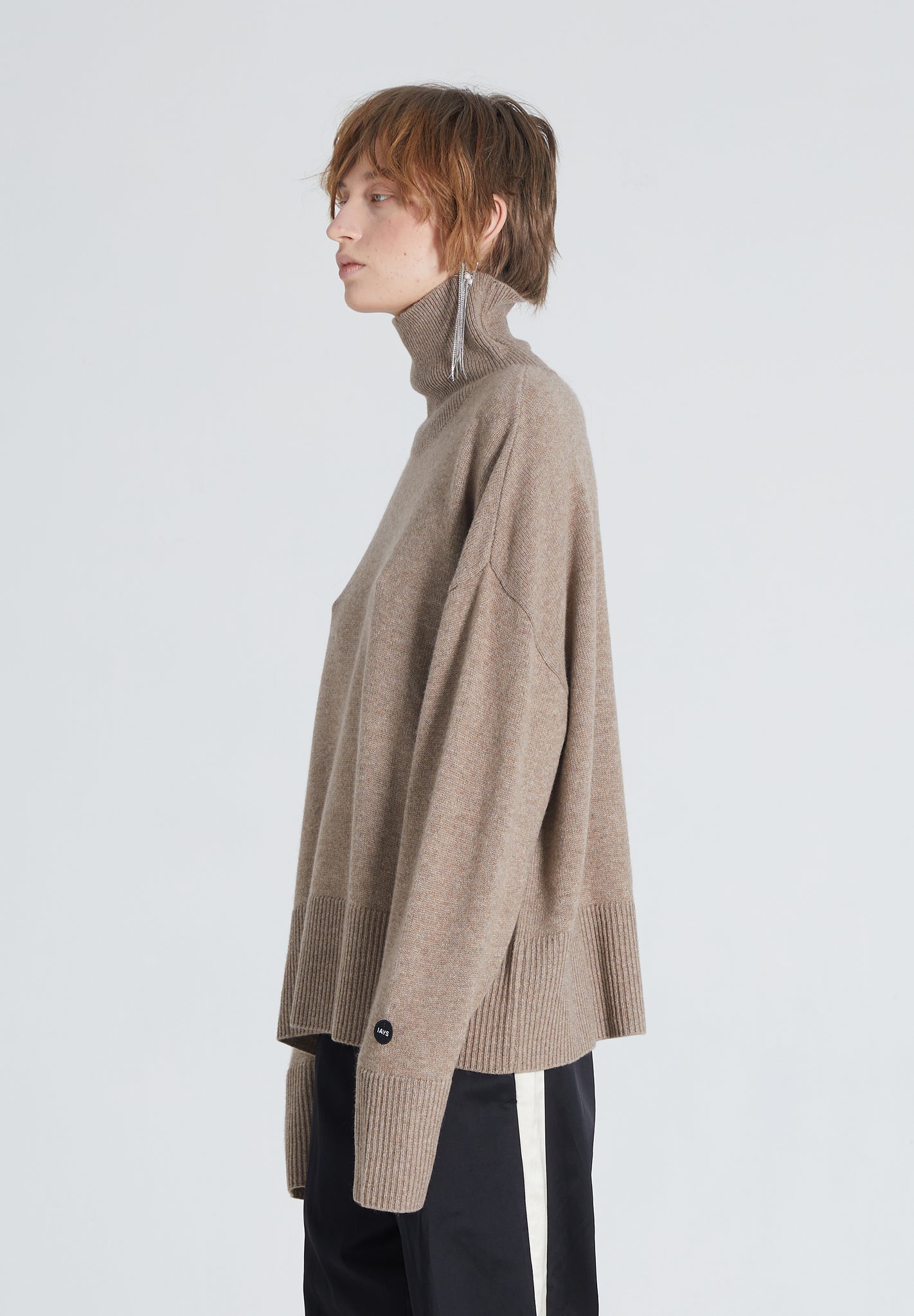 Woman wearing a high-end brown cashmere turtleneck. She also wears black pants and a silver earring 