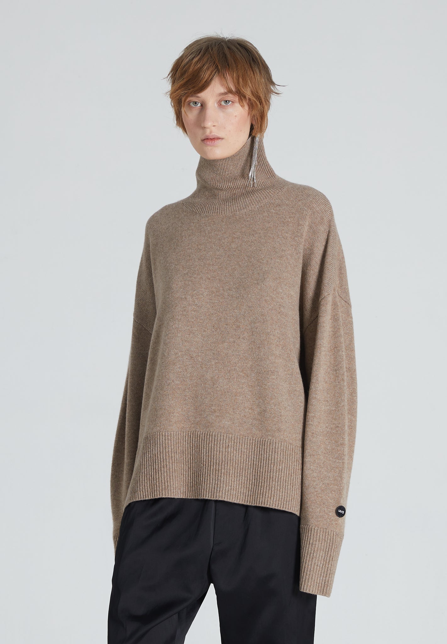 A woman wearing a brown turtleneck cashmere sweater and black trousers.