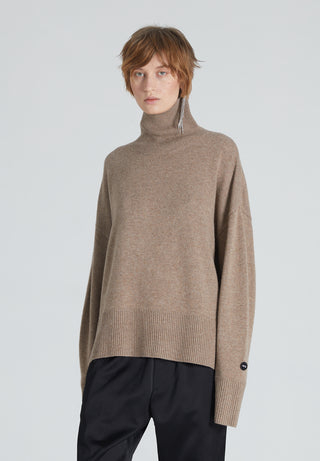 A woman wearing a brown turtleneck cashmere sweater and black trousers.