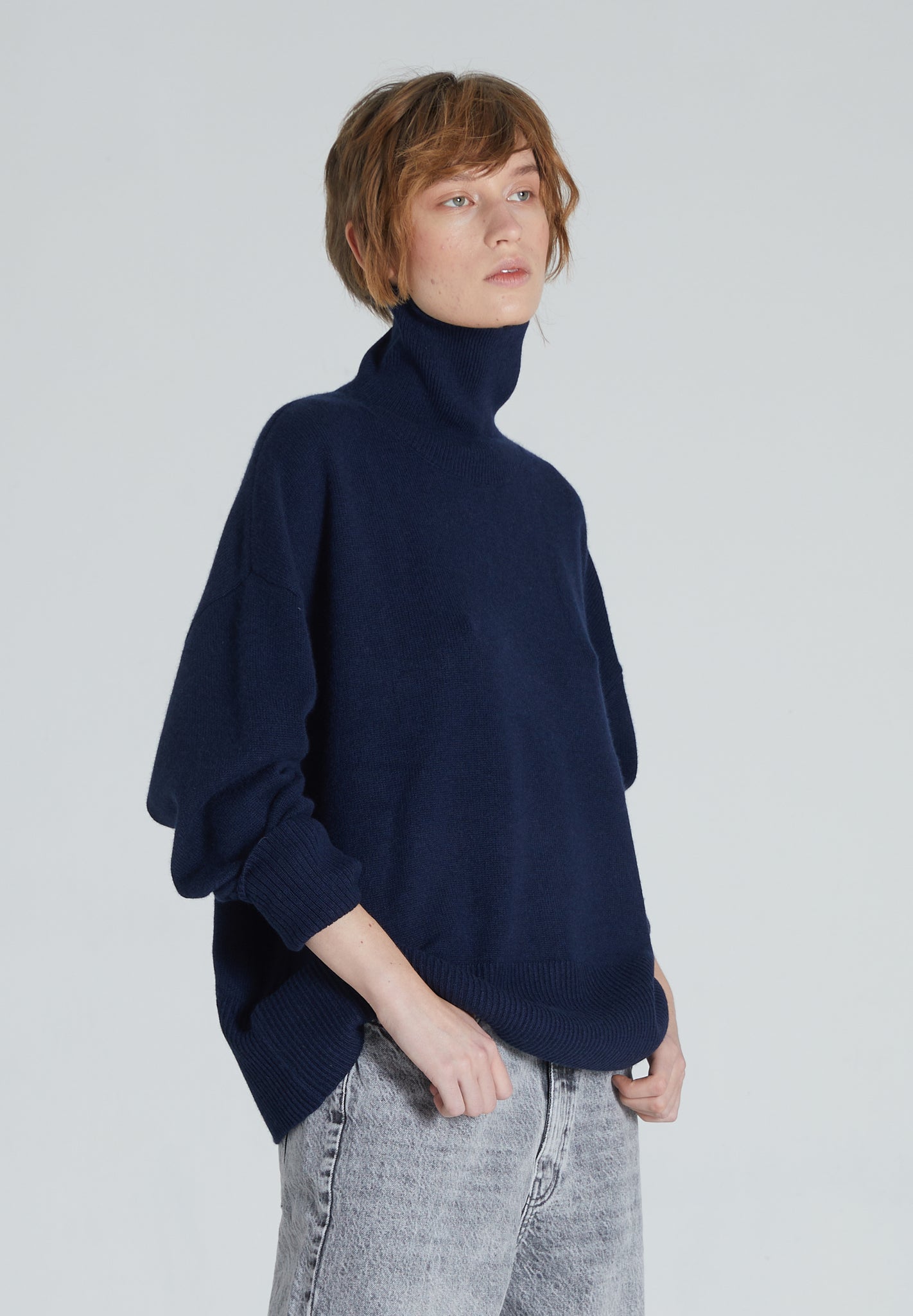 A woman wearing a navy cashmere turtleneck sweater with ribbed trims and a relaxed silhouette.